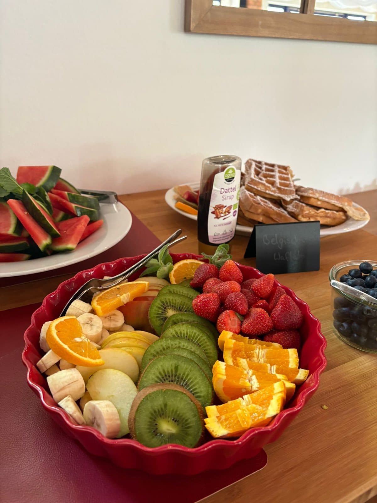 Obstschale mit Kiwi, Orange und Erdbeeren, dahinter frische Waffeln